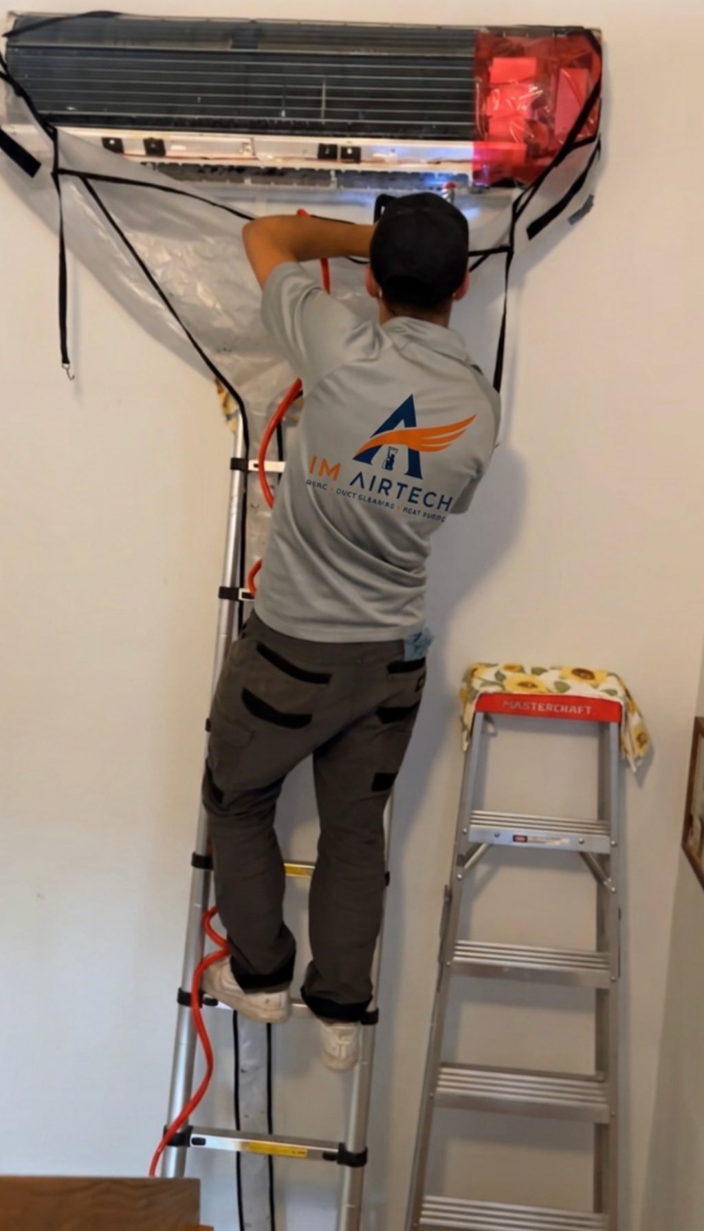 Technicien ImAirTech sur une échelle nettoyant une thermopompe murale avec une housse de nettoyage installée